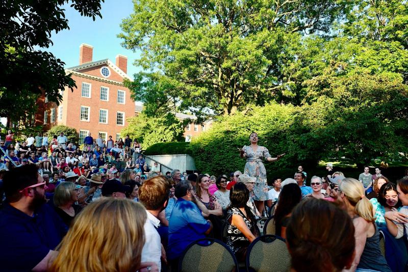 Woman standing in the middle of a crowd singing on a college campus.