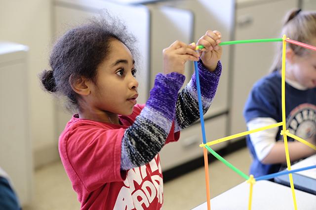 A little girl builds a structure from colored plastic straws