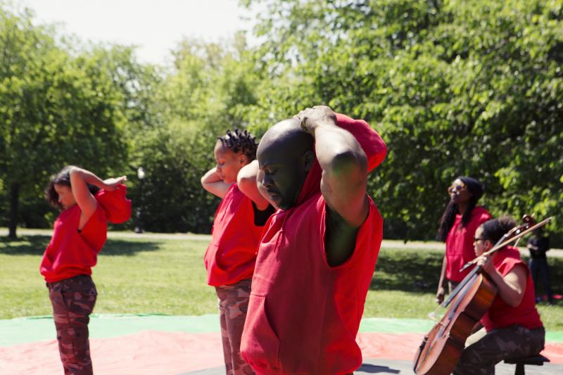 Group of people in red outfits, some with musical instruments, in Central Park. 