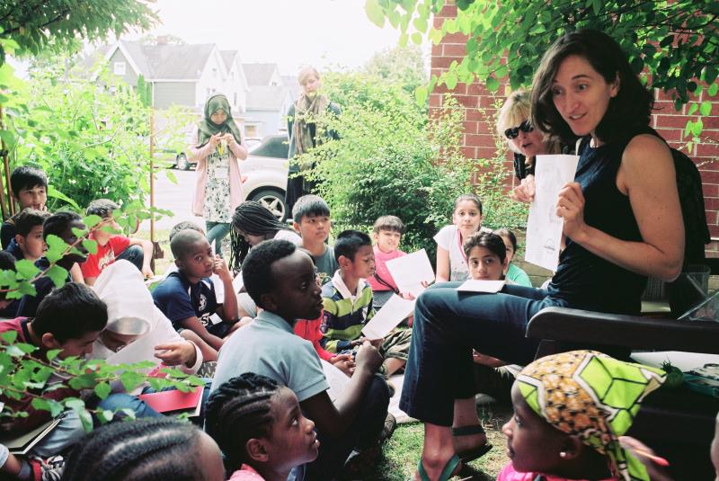 A woman shows students a worksheet while sitting in a garden