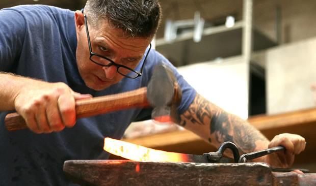 Closeup of a man hammering a red-hot strip of of metal