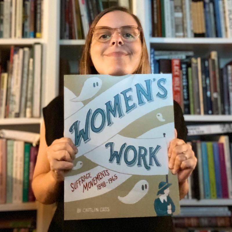 A woman with glasses holds up a book that says Women's Work
