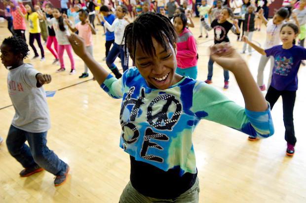 a young black woman wearing a shirt that says "LOVE" dances exuberantly with a group of students in street clothes