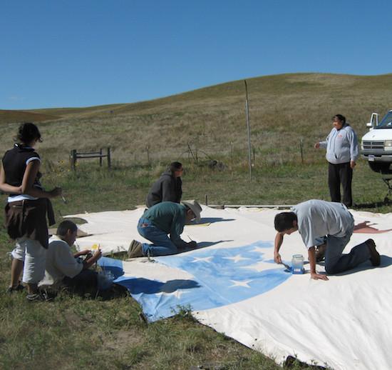 indigenous youth paint the walls of a tipi before it is assembled