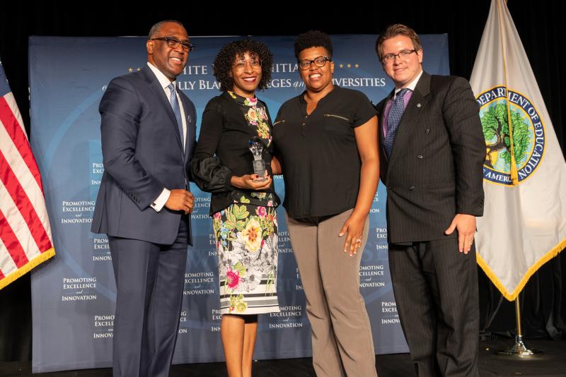 Man presenting award to two women and a man on stage. 