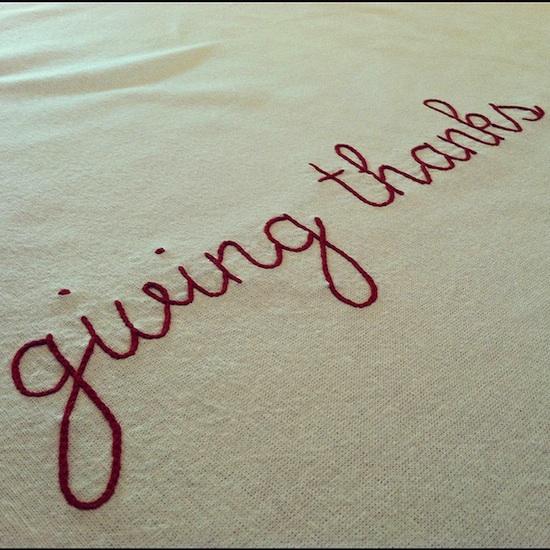 The phrase "giving thanks" embroidered in red thread on a white background