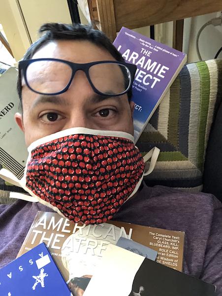 Greg Reiner sits wearing a COVID mask surrounded by playscripts