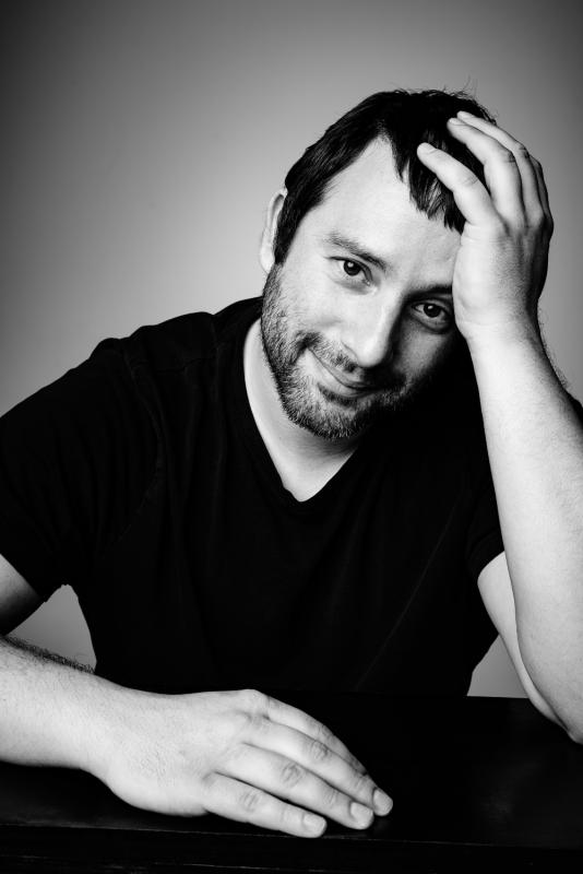 Playwright Itamar Moses Black and white photo of man in black shirt with head in hand