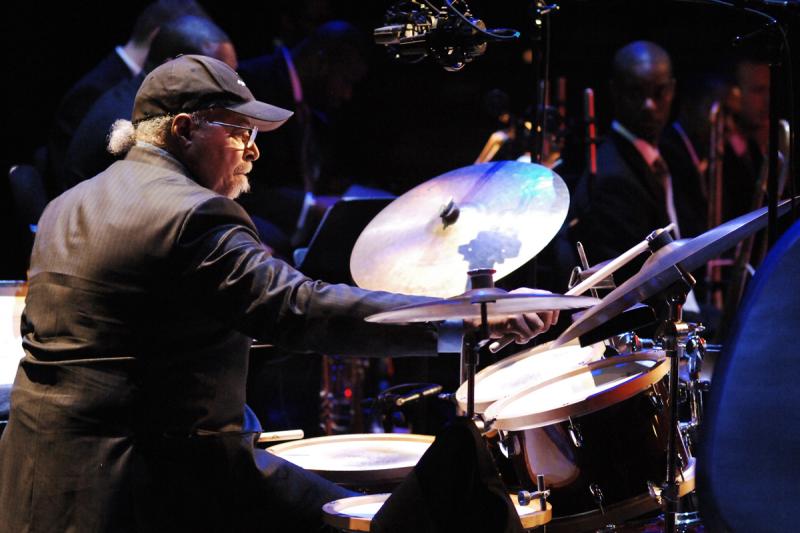 Jimmy Cobb A man wearing a black baseball hat plays the drums.