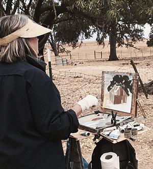 Woman working outdorrs on a paining of a farm scene