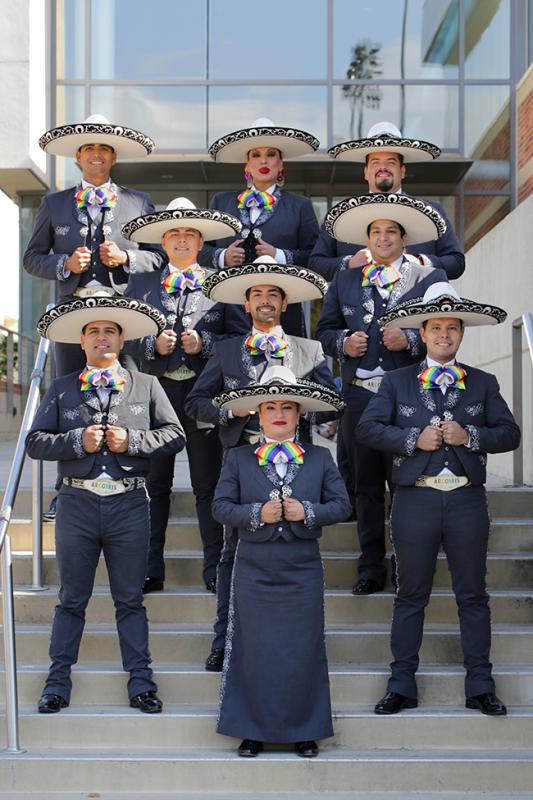 A mariachi band wearing rainbow bolo ties stands on steps of a building 
