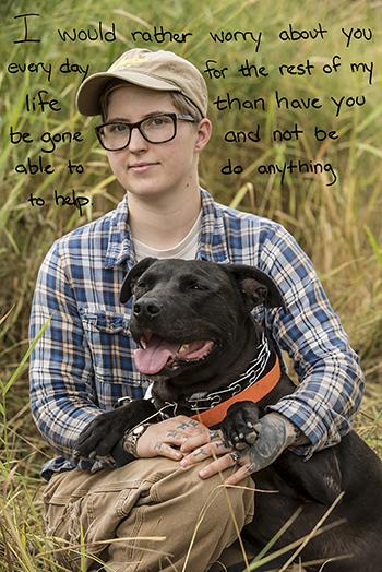 A woman sits while hugging a black dog