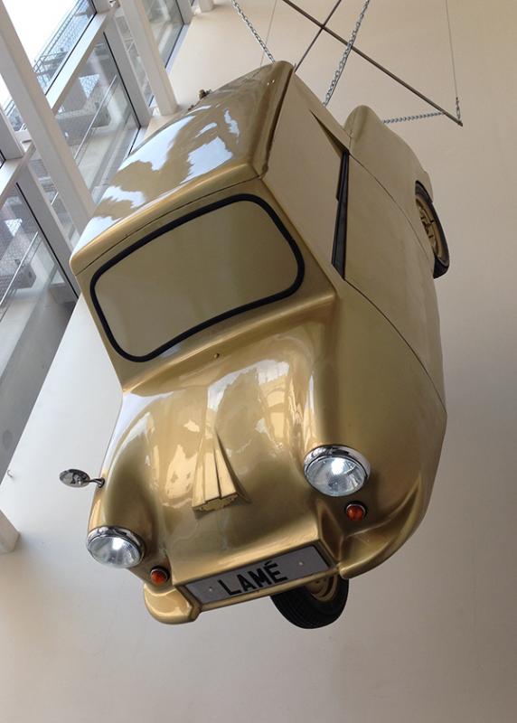 Gold Lame Gold car hanging from ceiling in museum.