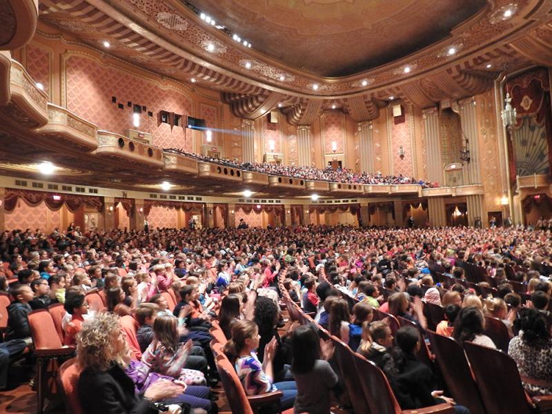 Young kids sitting in audience of performing center. 