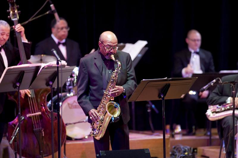 Man with glasses playing a saxophone. 