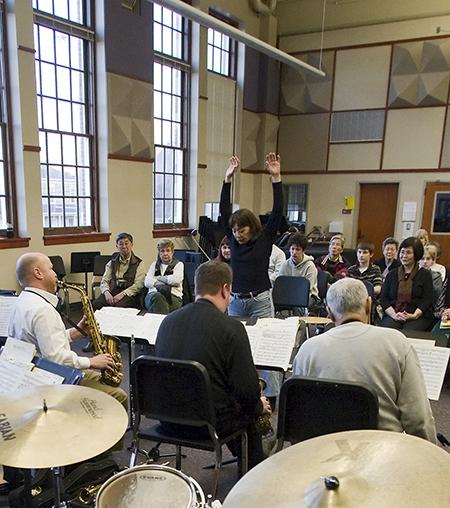 Asian woman raising arms in front of jazz orchestra.