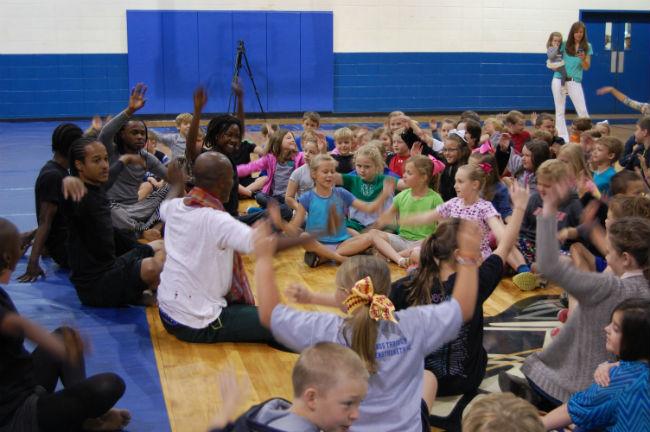 Dancers sit on floor leading a group of young children in movements