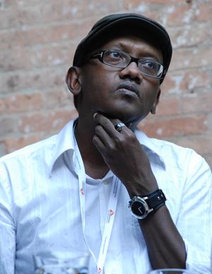African man wearing hat and glasses, hand on chin.