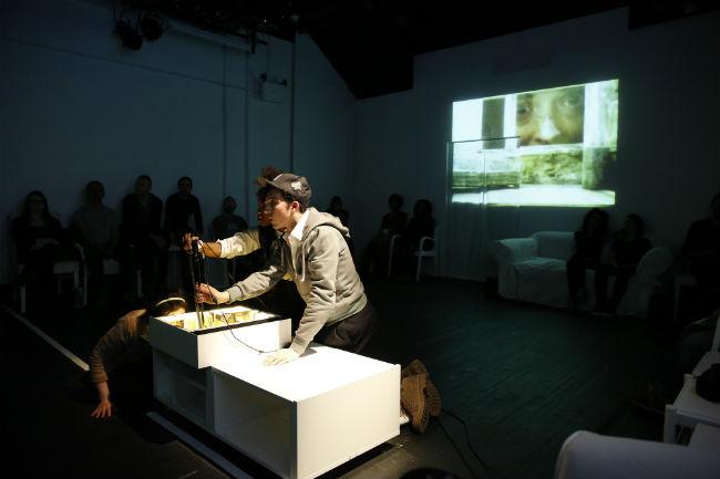 Act Two of Ludic Proxy by Aya Ogawa Two people in spotlight playing with a joystick