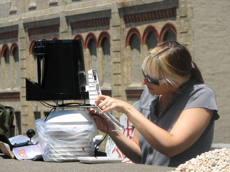 Andrea Polli Hello Weather! Woman in sunglasses putting together a piece of equipment.