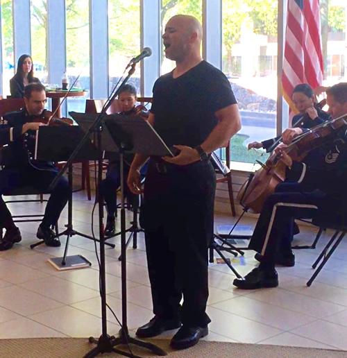 Man at a microphone singing with a small music ensemble behind