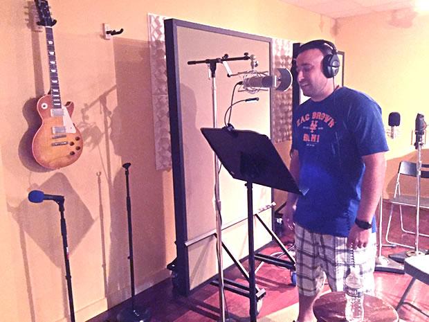 Man in a simple music studio with music stand in front of a professional recording microphone