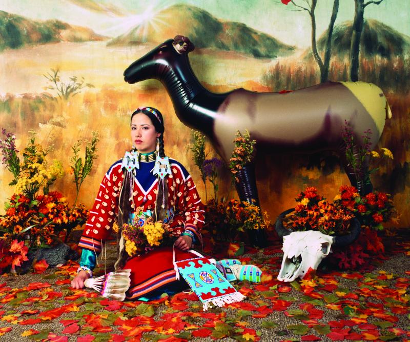 a woman sitting on the floor with the backdrop containing a field, flowers and a horse