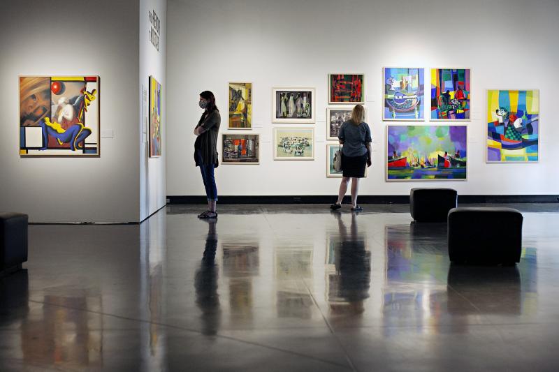 Two women look at a collection of abstract artwork on the walls of a gallery 