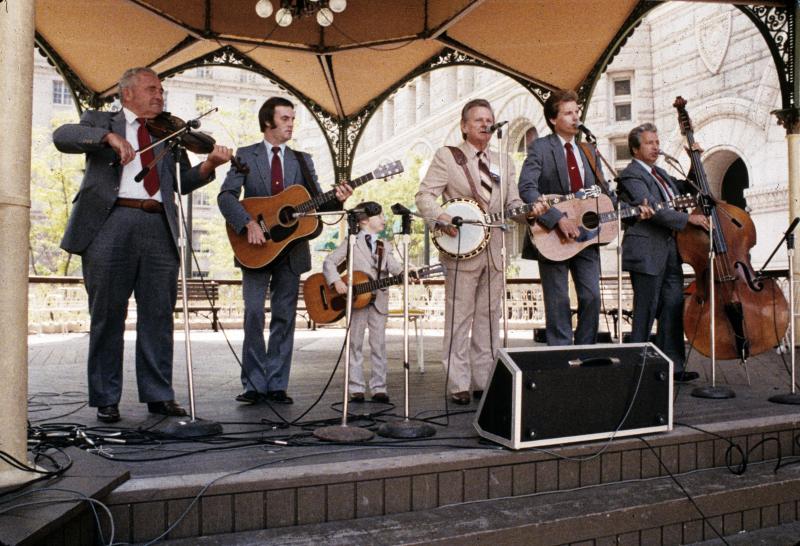 A five-piece bluegrass band, all white men wearing suits, on a stage playing. 