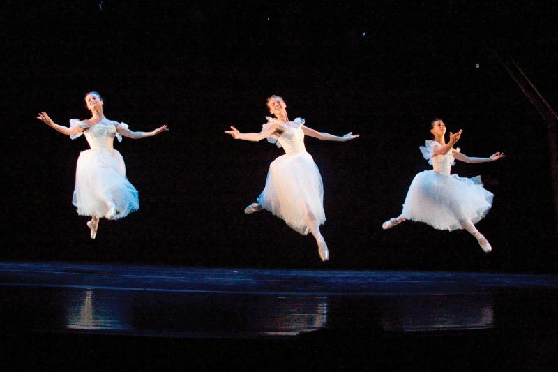Three women in long white dresses dancing on stage.