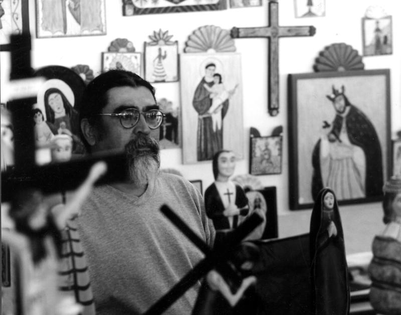 Man with glasses, dark hair, and gray goatee sitting in a studio with religious icons.