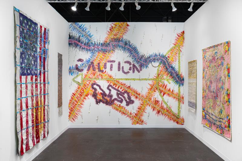 Art exhibit with artwork depicting the American flag (left), multi-colored artwork with the word CAUTION (middle), and two multi-colored fabric artwork (right)