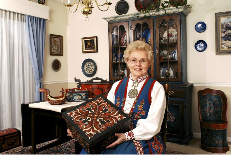 Eldrid Skjold Arntzen wearing traditional Norwegian clothing and holding a box with her floral designs painted on it. 