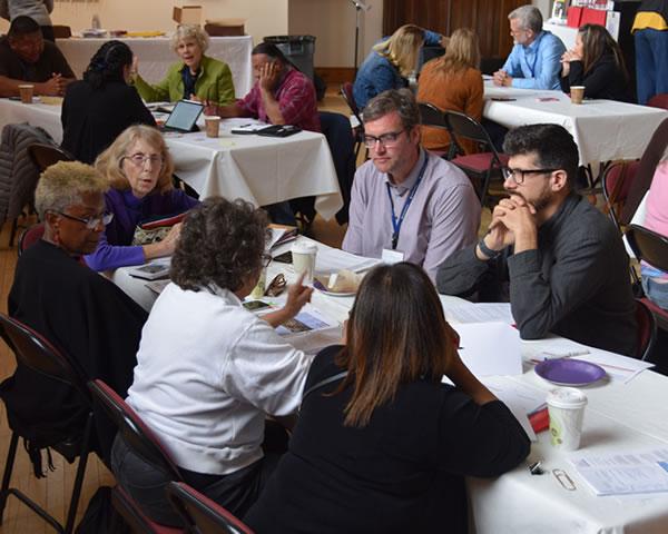 Large room with meeting attendees at tables working on a common project