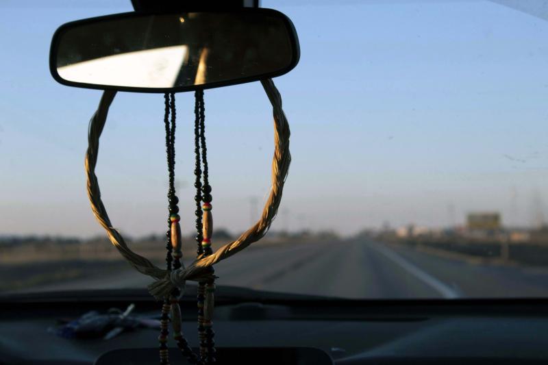 A braided sweetgrass ring and beads hang from a rearview mirror