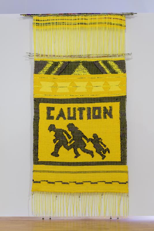 Yellow and black fabric art with the words CAUTION across it and three figures walking