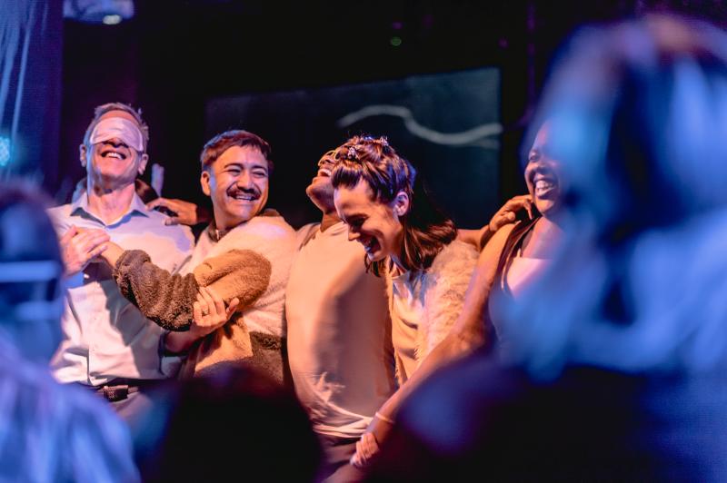 A group of for people stand with their arms around each other smiling