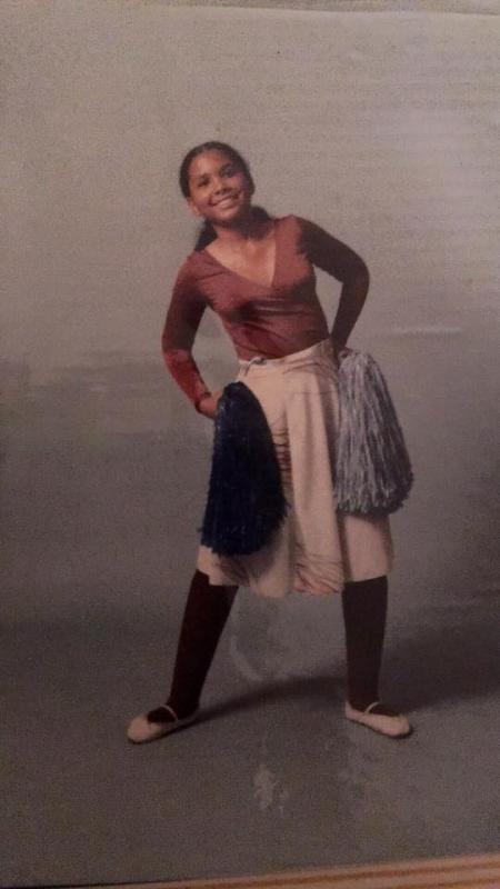 Dancing An adolescent girl smiles while holding pom poms and wearing ballet slippers, leotard, and dance skirt