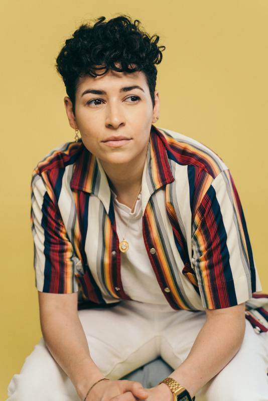 Denice Frohman, who is a woman with curly hair. She is seated and wearing a colorful striped shirt