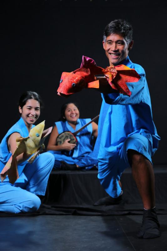 The Carp Who Would Not Quit Actors dressed in flowing blue outfits hold fish puppets and a banjo while performing a traditional Japanese fable