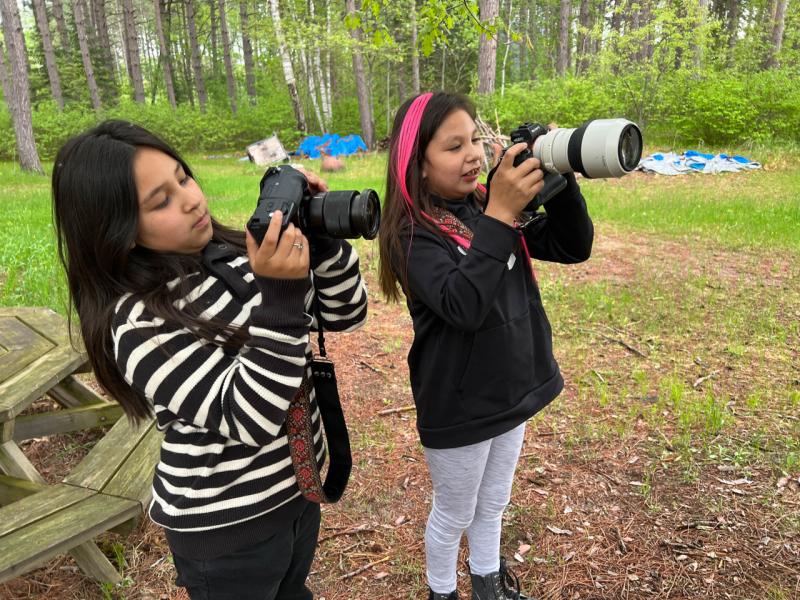 Two students hold large digital cameras in an outdoor setting 