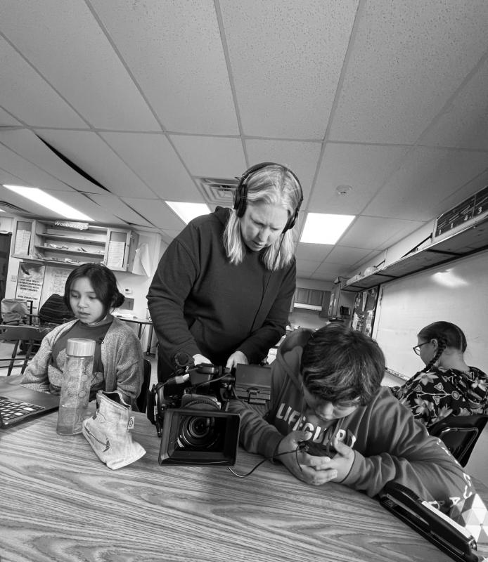 An woman stands over a camera in between two students