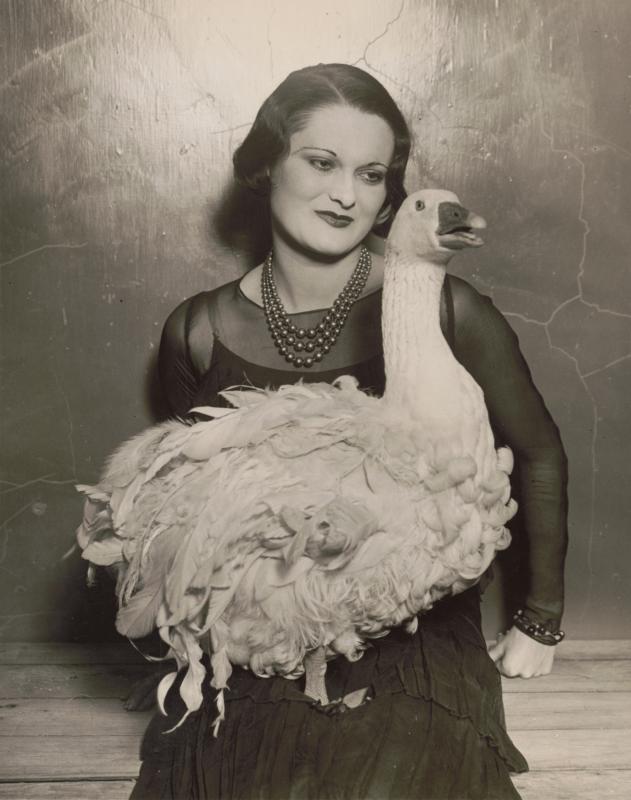Black and white photo of woman sitting and smiling at a goose in her lap. 