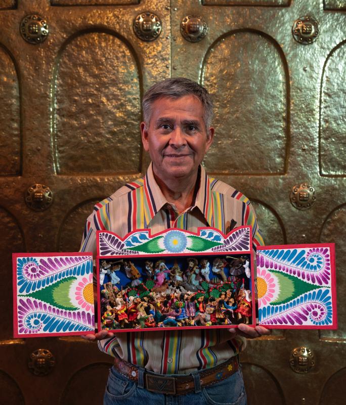 Jeronimo Lozano photo courtesy of © Glencairn Museum, Bryn Athyn, Pennsylvania.jpeg A man with grey hair stands holding a display of colorful figurines set in a hand-painted Nativity box