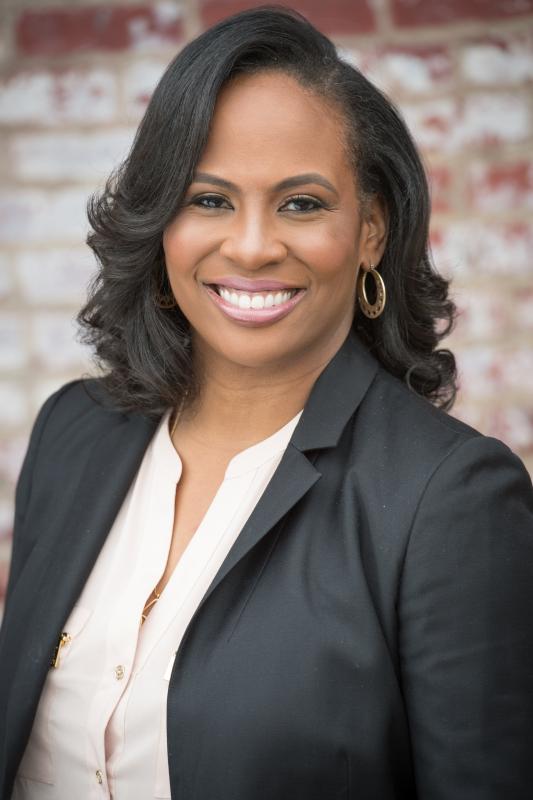 Portrait of Black woman with long dark hair wearing a dark suitcoat and white shirt. 