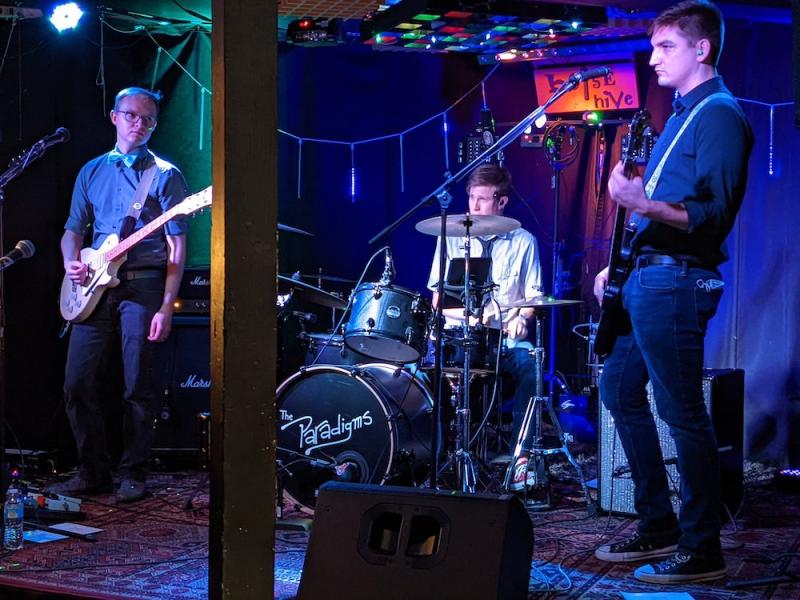 Three men who are members of a band stand onstage ready to perform