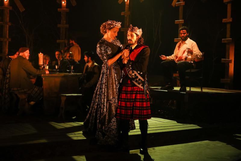 Actors playing Macbeth and Lady Macbeth stand together on stage colluding