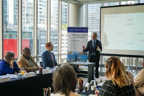 a group of people around a table listening to someone speaking in front of a whiteboard