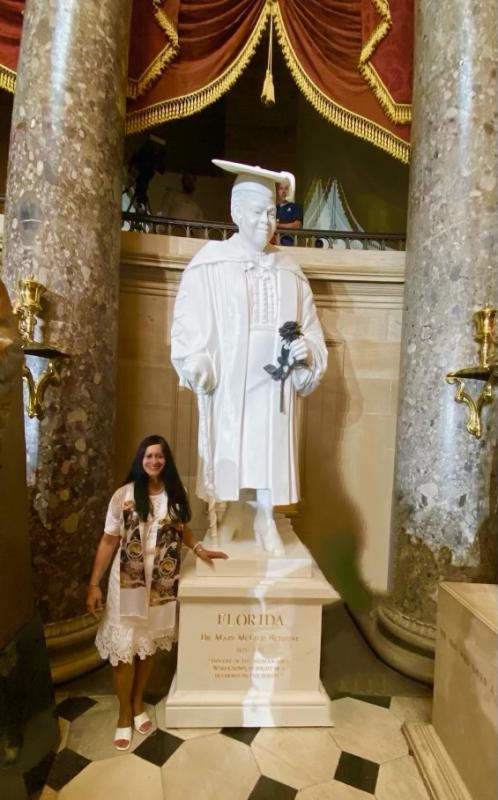 Woman with long black hair standing by her white marble sculpture of Dr. Bethune holding a black rose.