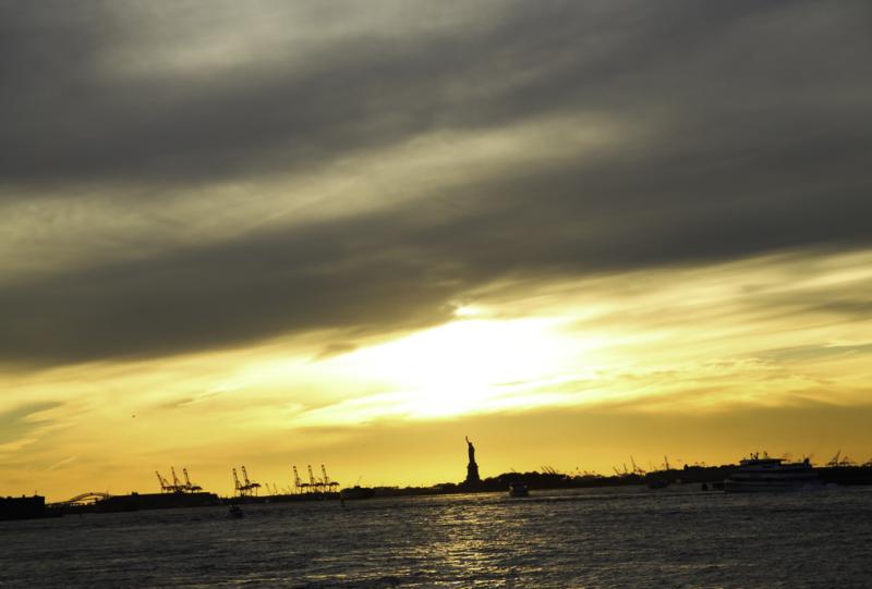 the sun sets with a view of the statue of liberty in the background